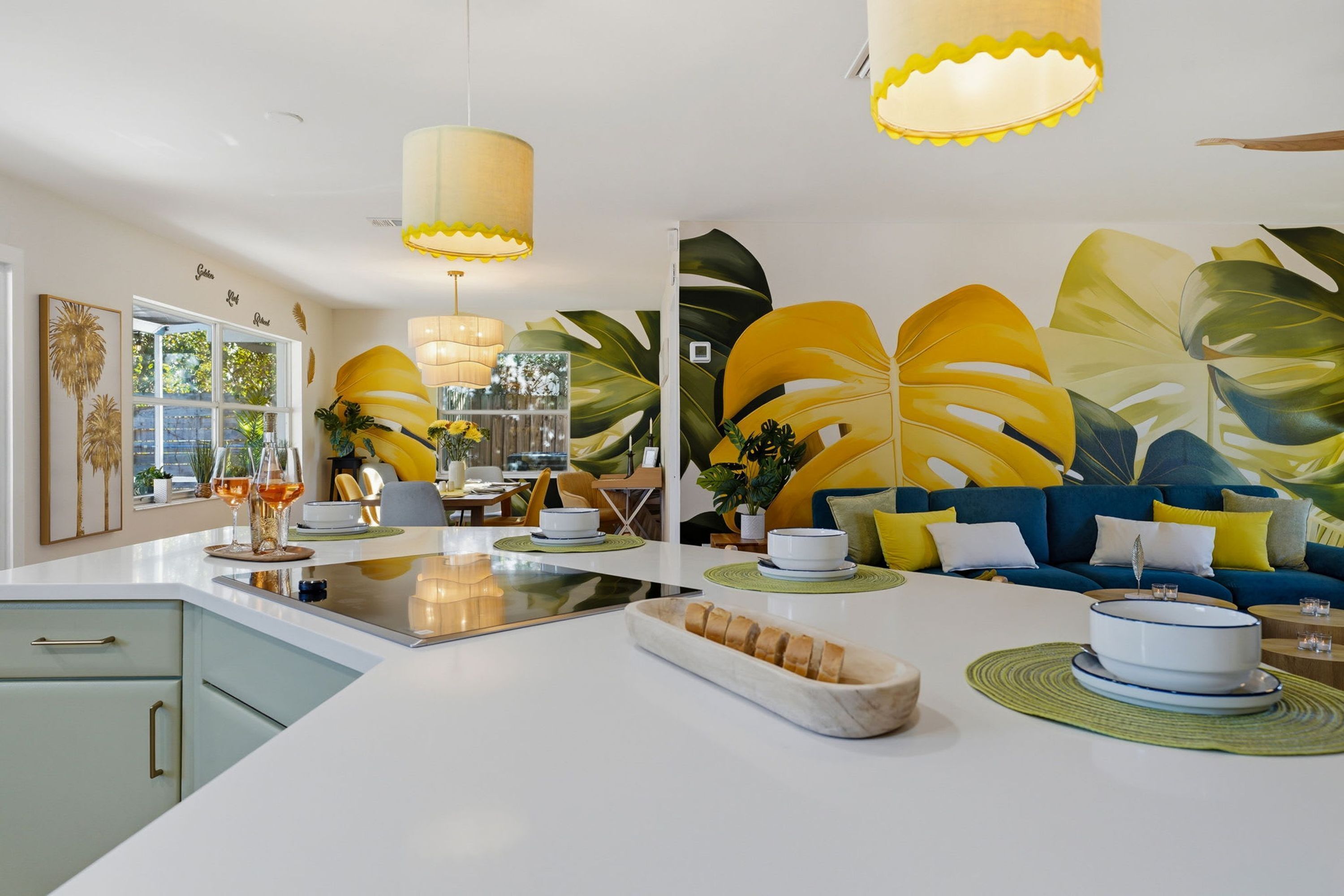 Een moderne keuken met een centraal eiland, een eethoek met gele stoelen en een grote blauwe bank met gele kussens.