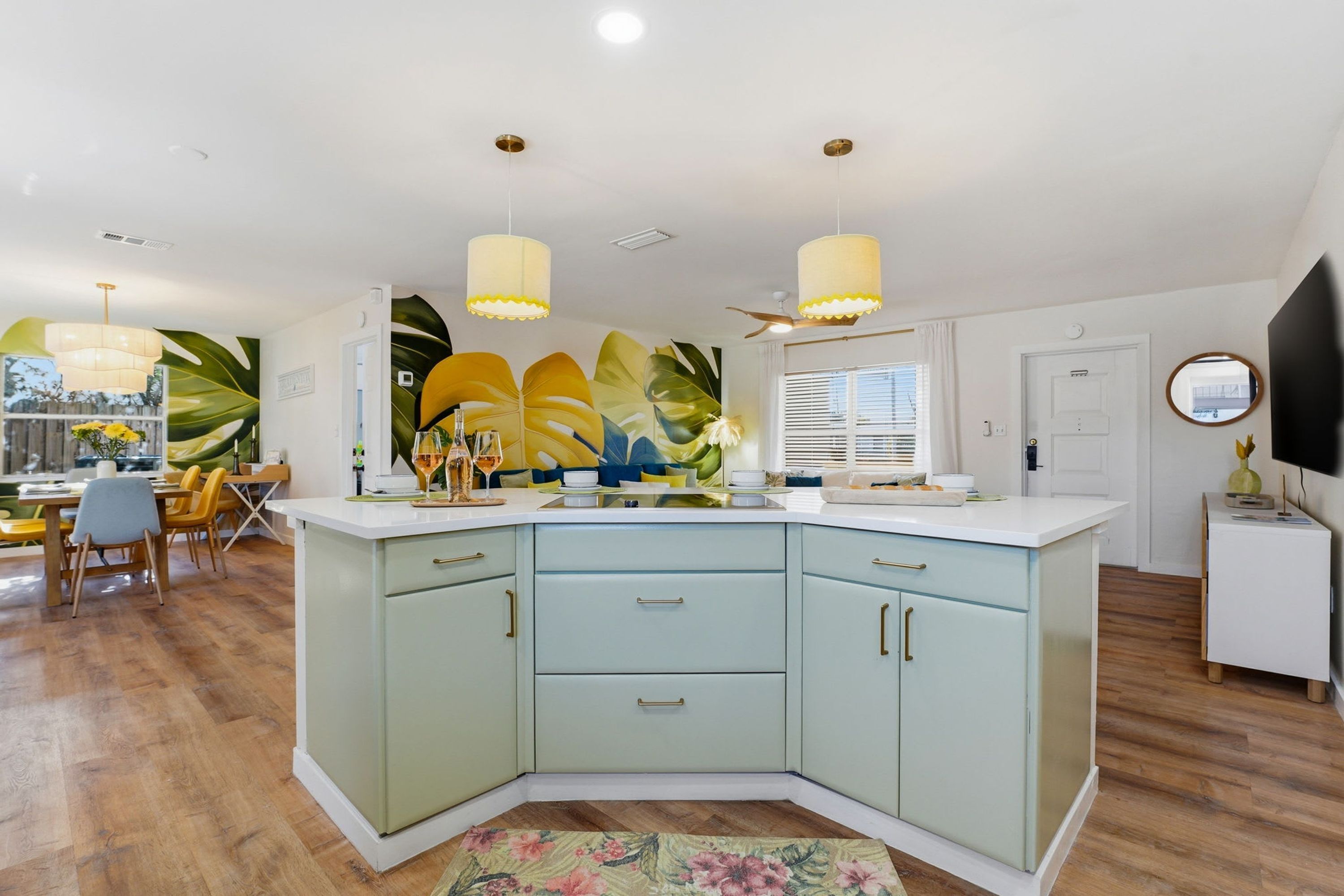 A modern kitchen with a curved island, wooden flooring, and pendant lighting.