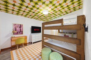Una habitación con literas, un escritorio con un televisor mostrando 'NETFLIX', una silla y un piso con diseño.
