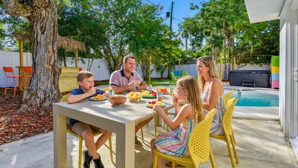 En familj äter middag utomhus med en pool i bakgrunden.