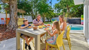 Una familia cenando al aire libre, con una piscina al fondo.