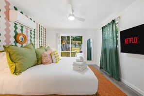 A hotel room with a bed, pillows, a ceiling fan, a TV screen, and a view of an outdoor area. - Backyard Oasis Heated Pool Tiki Bar Hot Tub (Largo)