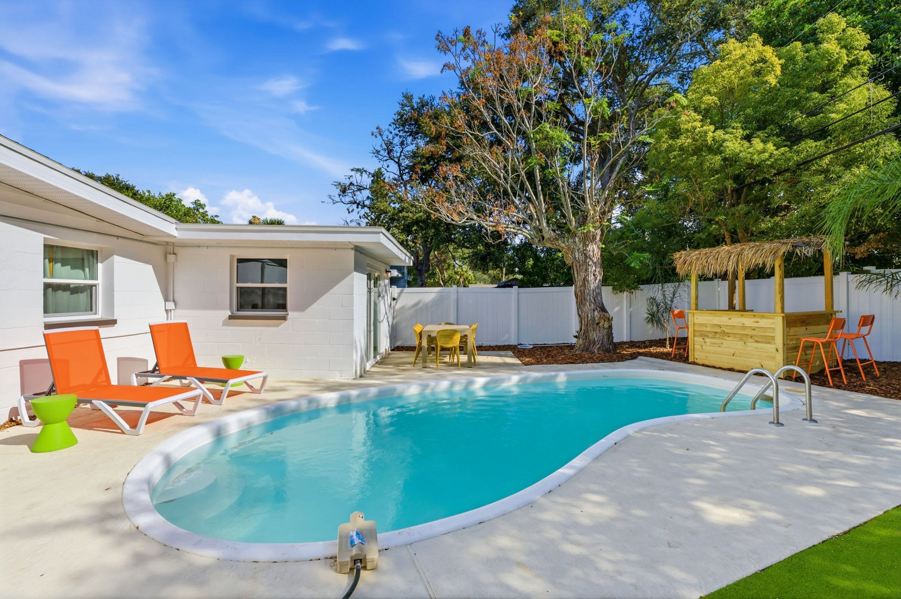 Un patio trasero con piscina, mobiliario exterior y un árbol.