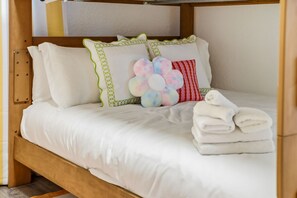 Un letto singolo con biancheria bianca, cuscini verdi e rossi e un cuscino decorativo con motivo floreale, oltre a una pila di asciugamani piegati.