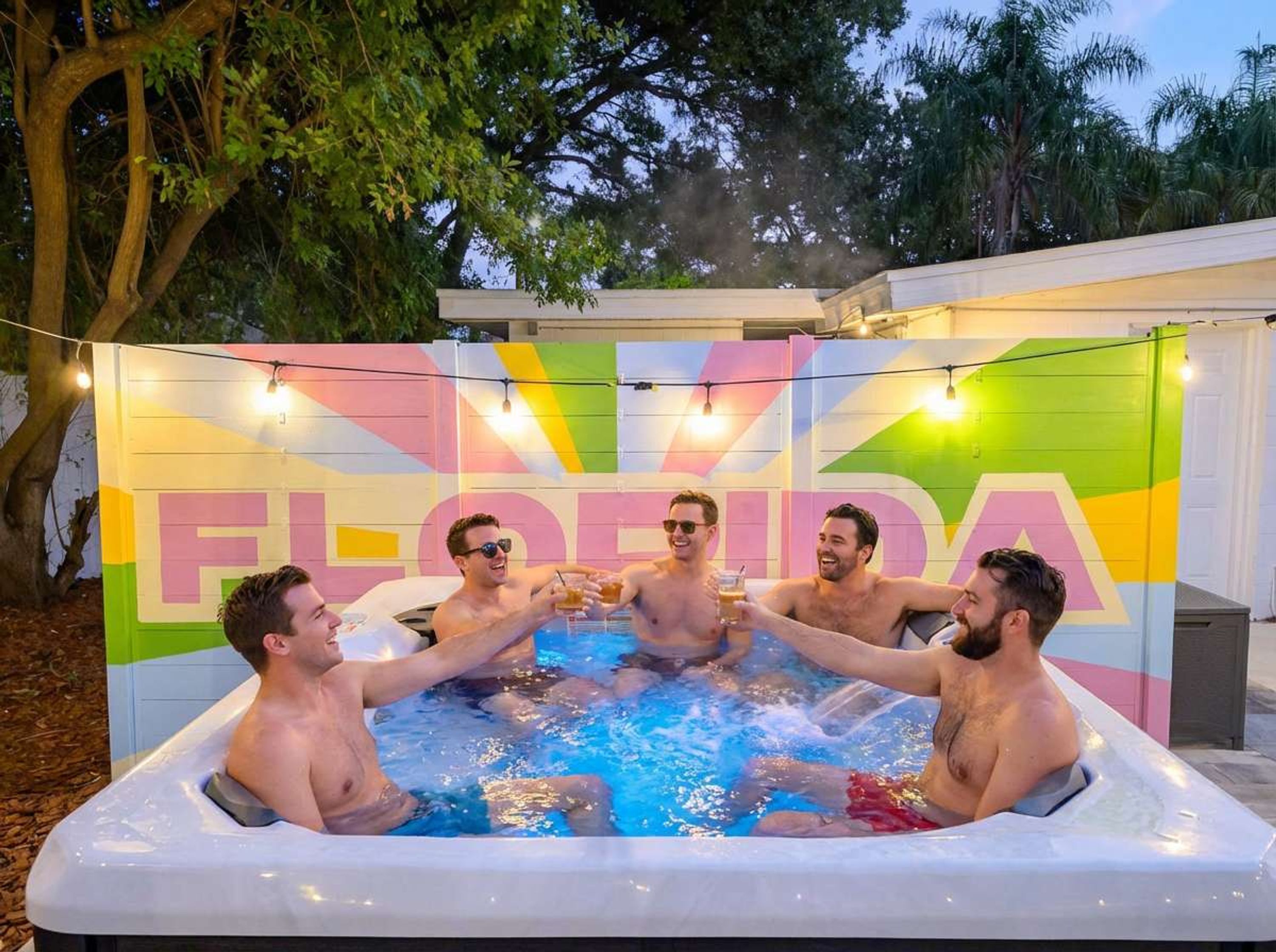 Un groupe de personnes dans un jacuzzi, avec en arrière-plan un décor coloré sur lequel on peut lire le mot « FLORIDE ».