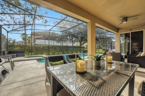 Eine überdachte Terrasse im Freien mit einem Glastisch, Korbmöbeln und einem Pool.