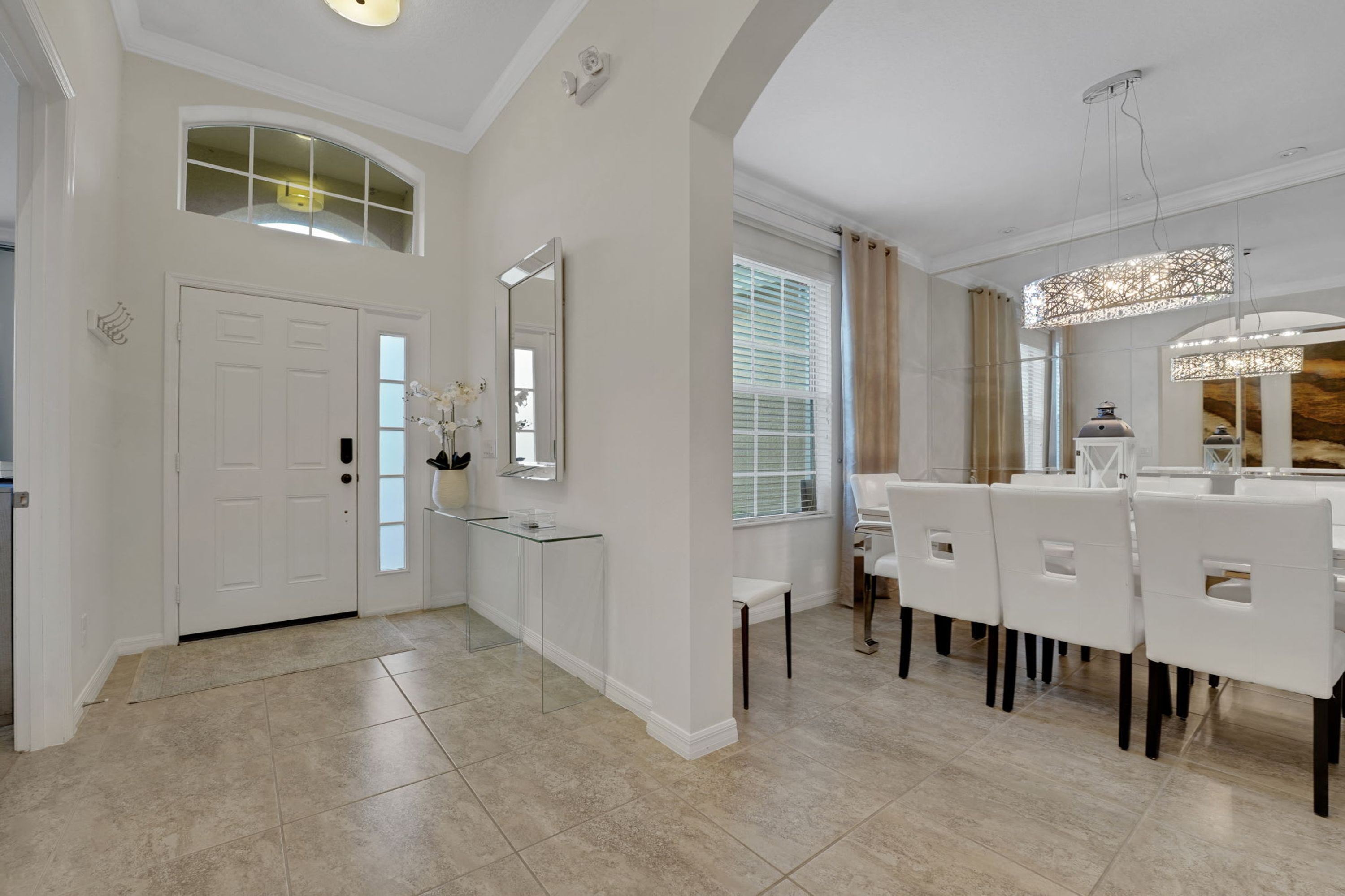 A modern interior with a glass partition, a dining area with white chairs, and a large mirror.
