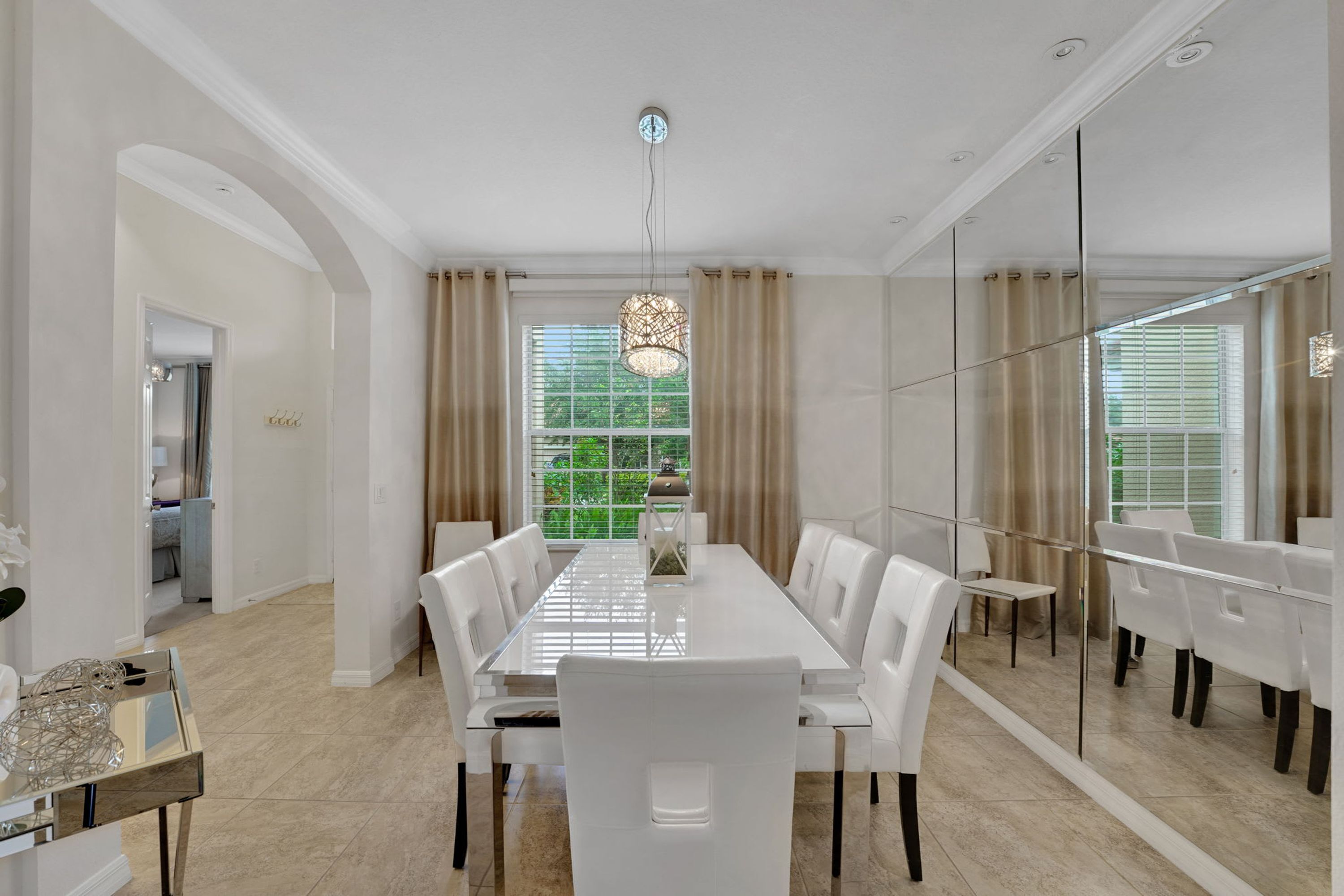 Una sala da pranzo moderna con un lungo tavolo e sedie bianche, ampie finestre con tende e un lampadario.