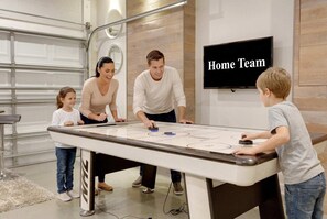 A family playing shuffleboard in a modern indoor setting with a TV labeled 'Home Team' in the background. - Family Escape - Pool Games Dog-friendly (Davenport)