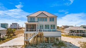 Una casa frente al mar de dos pisos con balcón, terraza de madera y vista al océano.