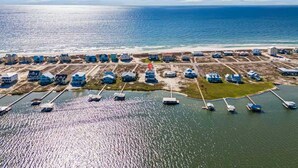 Vista aérea de una zona costera con varios edificios, un puerto deportivo con barcos y una playa.