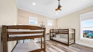 Habitación con dos literas, piso de madera, ventilador de techo y ventana con vistas.