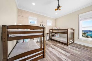 A room with two bunk beds, wooden flooring, a ceiling fan, and a window with a view. - Gulf Shores Retreat Heated Pool Lagoon 4BR (Gulf Shores)