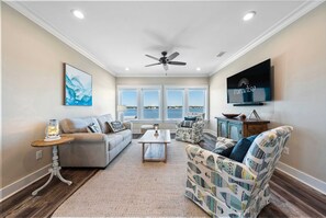 A living room with a sofa, armchair, coffee table, and a television mounted on the wall. - Gulf Shores Retreat Heated Pool Lagoon 4BR (Gulf Shores)
