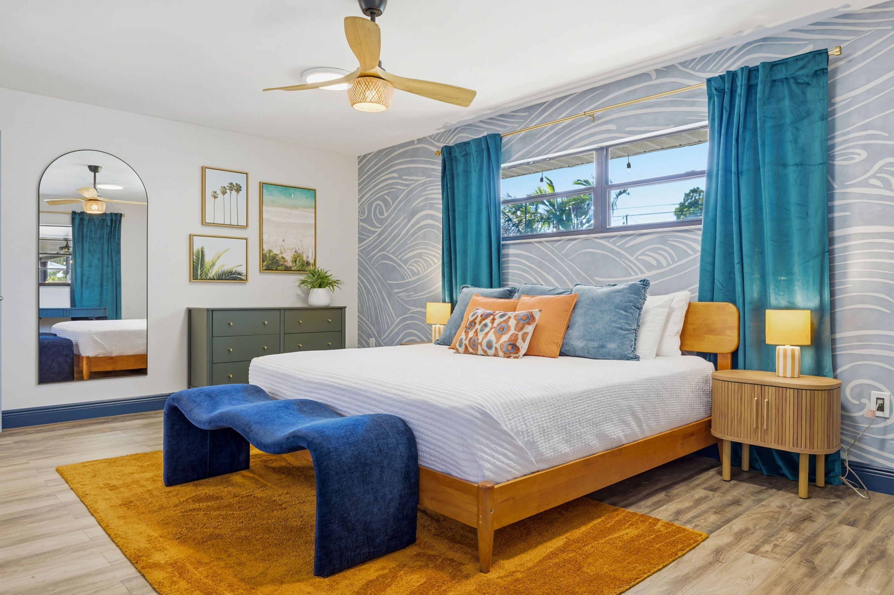 A bedroom with a bed, bedside tables, a bench, a ceiling fan, and a window with curtains.