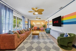 Ein Wohnzimmer mit Sofa, Sesseln, Couchtisch, Fernseher und Deckenventilator.