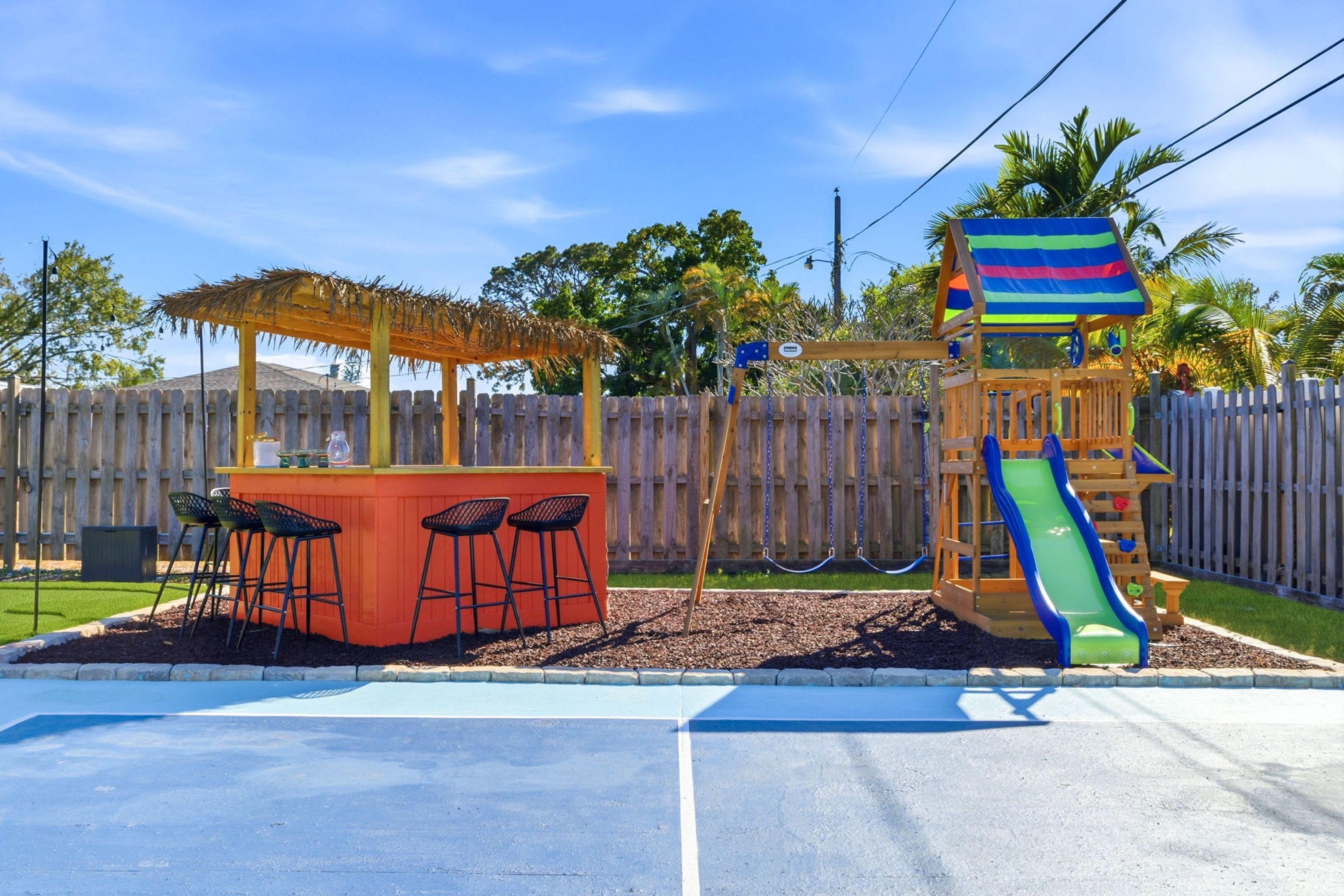 A playground with a slide, swings, and a small bar area with chairs.