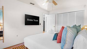 Un dormitorio con cama, almohadas, televisor, ventilador de techo y una puerta.