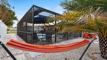 Un área de piscina moderna al aire libre con una hamaca, sillones reclinables y un espacio de descanso techado.