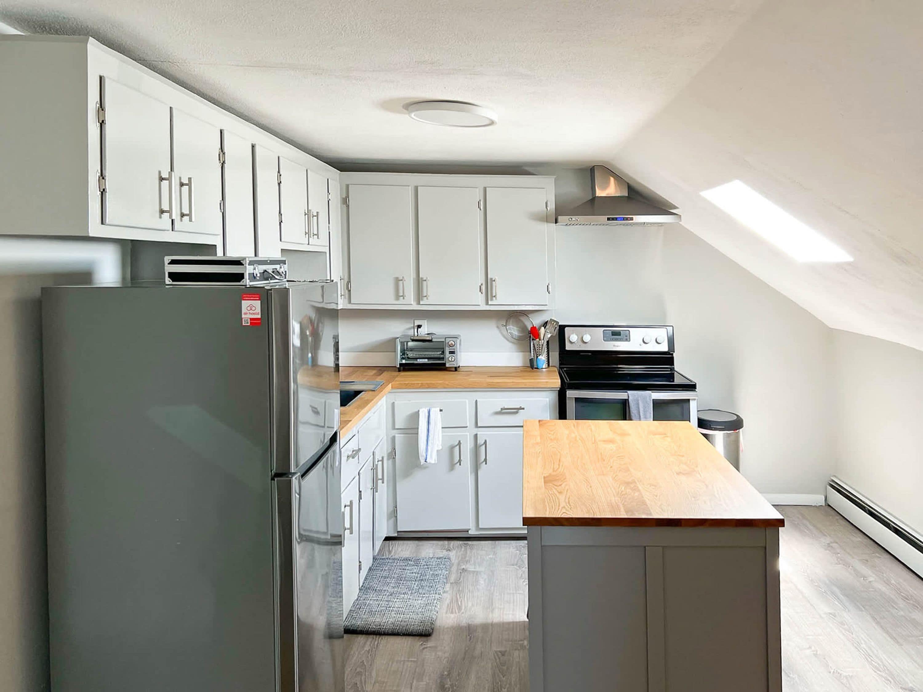 A modern kitchen with white cabinets, a stainless steel refrigerator, a built-in oven, and a wooden countertop.