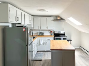 Eine moderne Küche mit weißen Schränken, einem Edelstahl-Kühlschrank, einem eingebauten Ofen und einer Holz Arbeitsplatte.