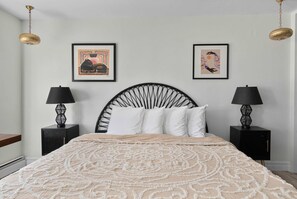 Ein Schlafzimmer mit einem Bett, zwei Nachttischen, zwei Lampen und zwei gerahmten Kunstwerken an der Wand.