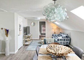 Ein modernes Wohnzimmer mit Fernseher, Sitzgelegenheit und einem außergewöhnlichen Glaskandelaber.