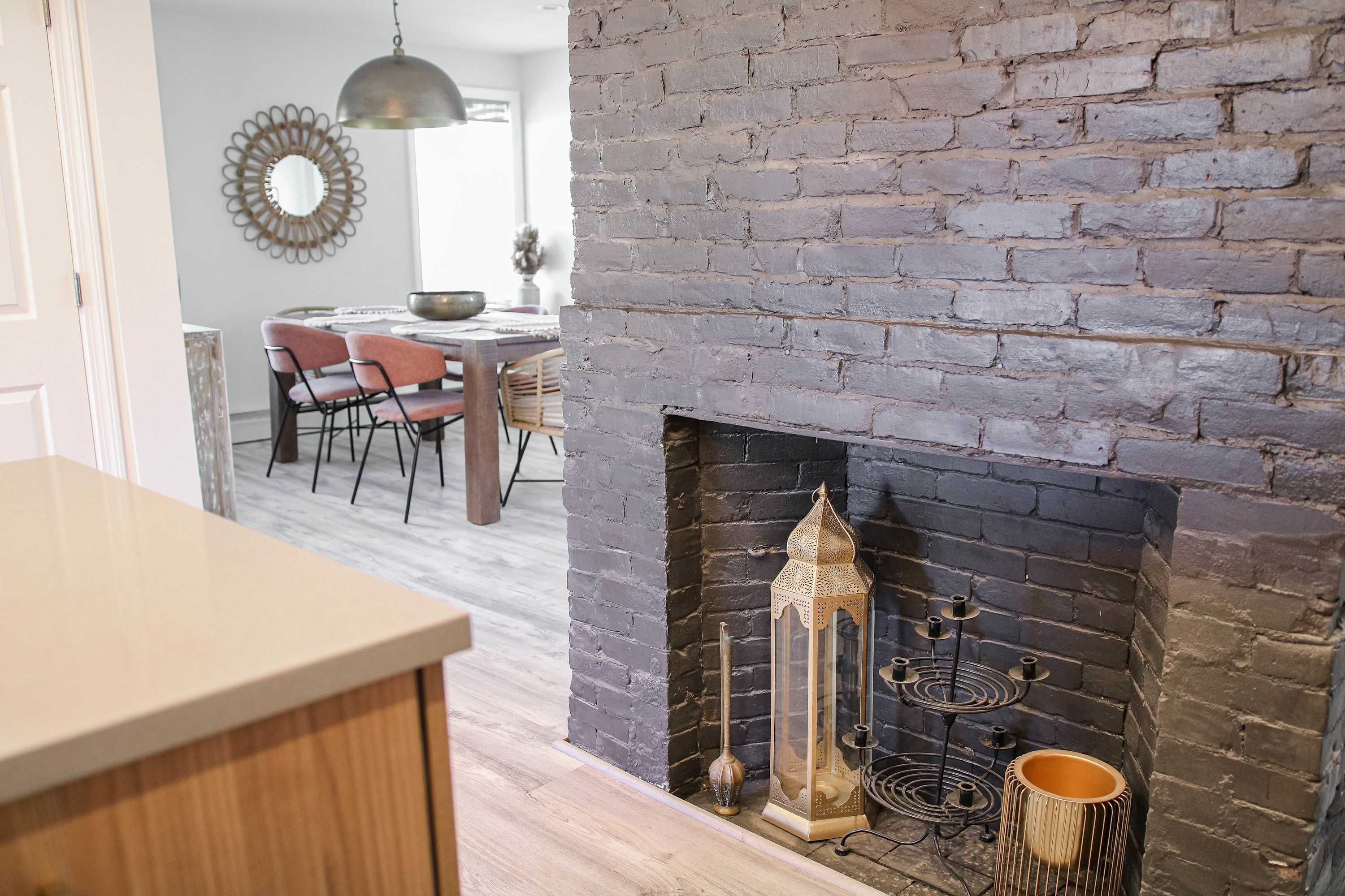 A kitchen with a brick fireplace, a dining area with chairs and a table, and a hanging pendant light.