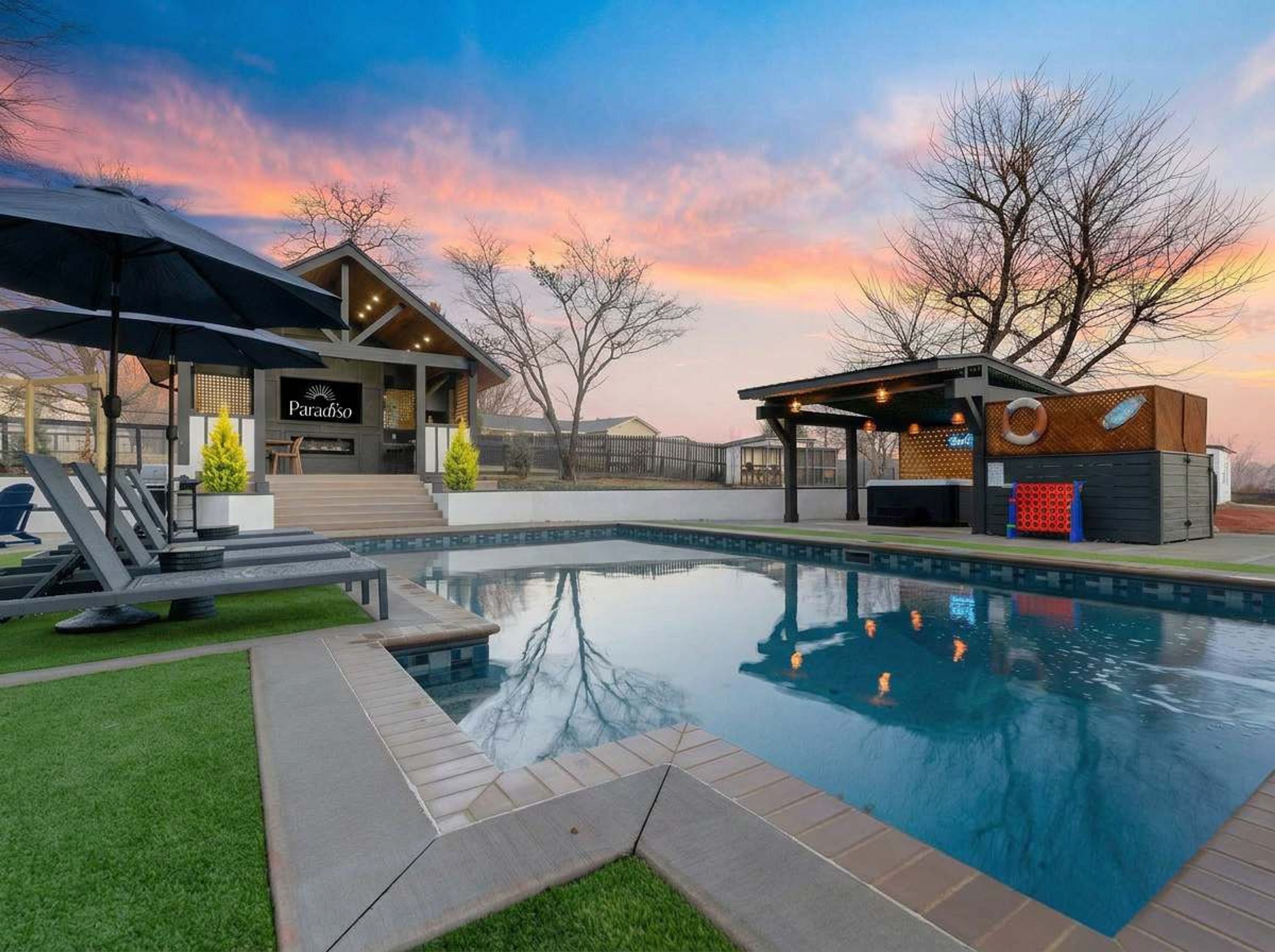 A modern outdoor pool area with a lounge chair, a covered seating area, and a building with a sign.