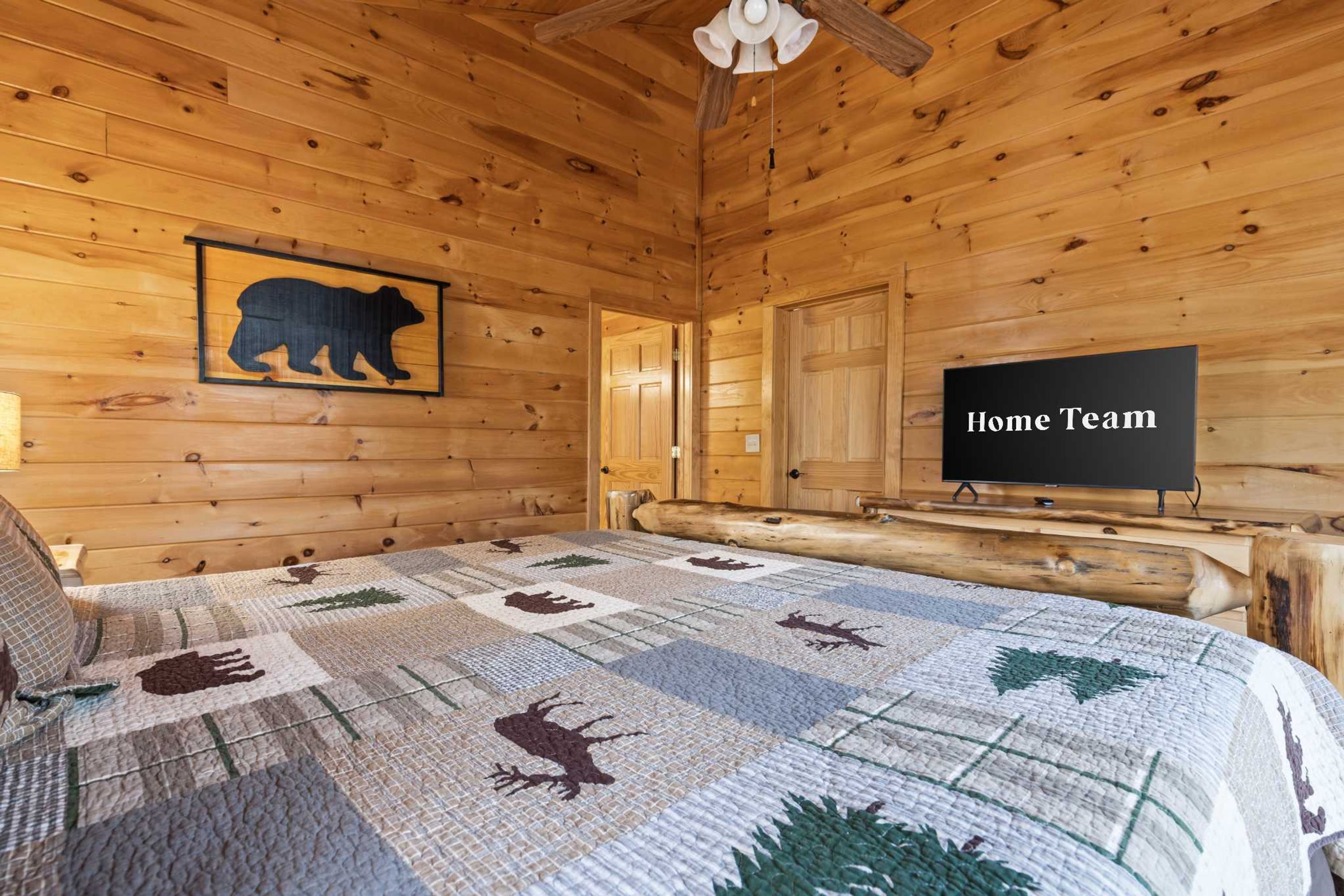 A log cabin room with a bed, a bear silhouette on the wall, a television, and a quilt with animal prints.