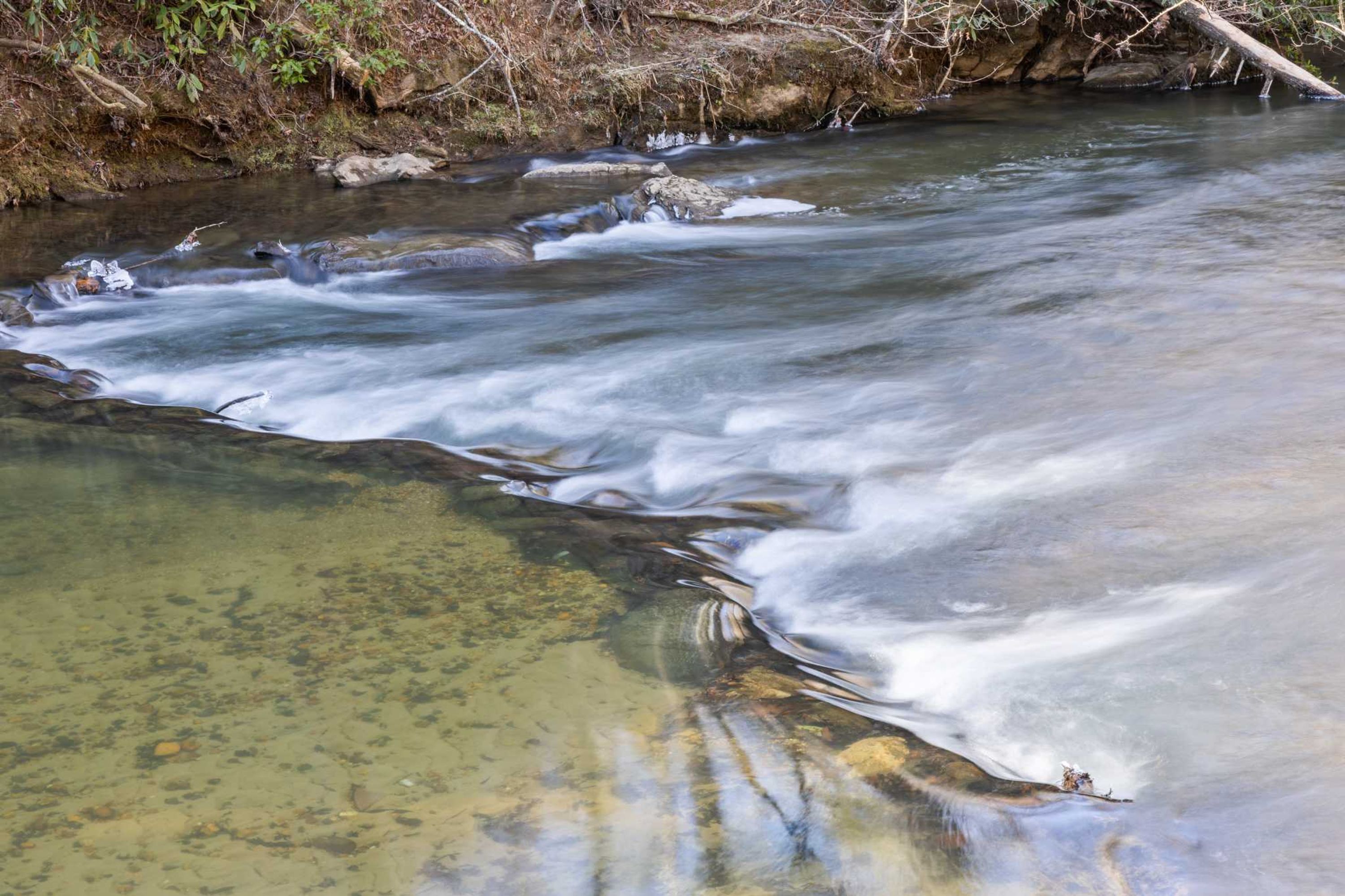 A clear stream with visible rocks and a natural environment.
