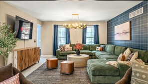 A modern living room with a sectional sofa, a coffee table, and a television mounted on the wall. - Epic Poconos Pad Pool Hot Tub Gym Golf Sim (East Stroudsburg)