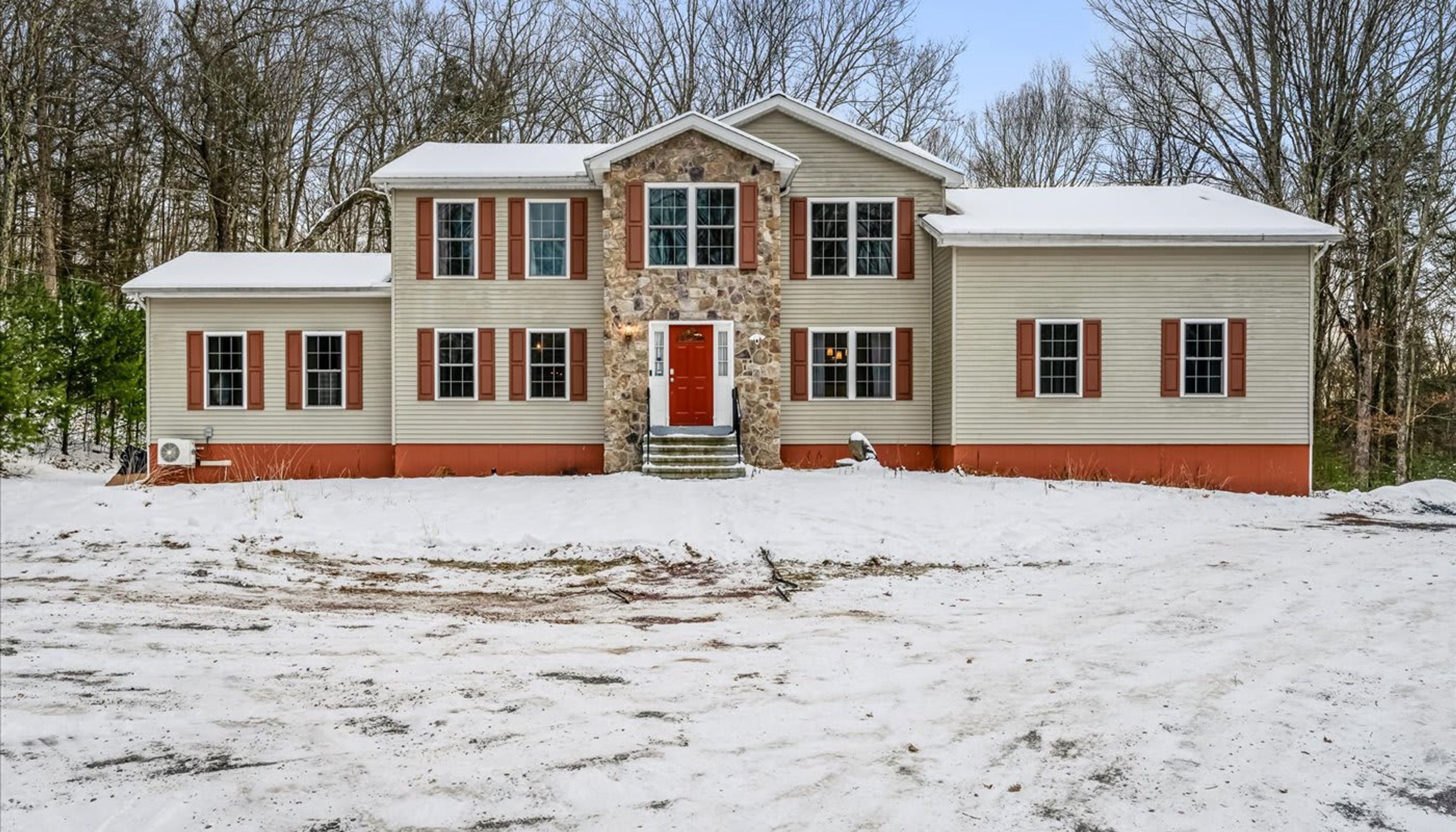 A two-story house with a stone entrance and red shutters, surrounded by snow.