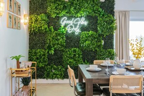 A dining area with a wall of green foliage and a neon sign that reads 'Good Vibes Only.' - Heated Pool Game Room Putt Putt Pet Friendly (Largo)