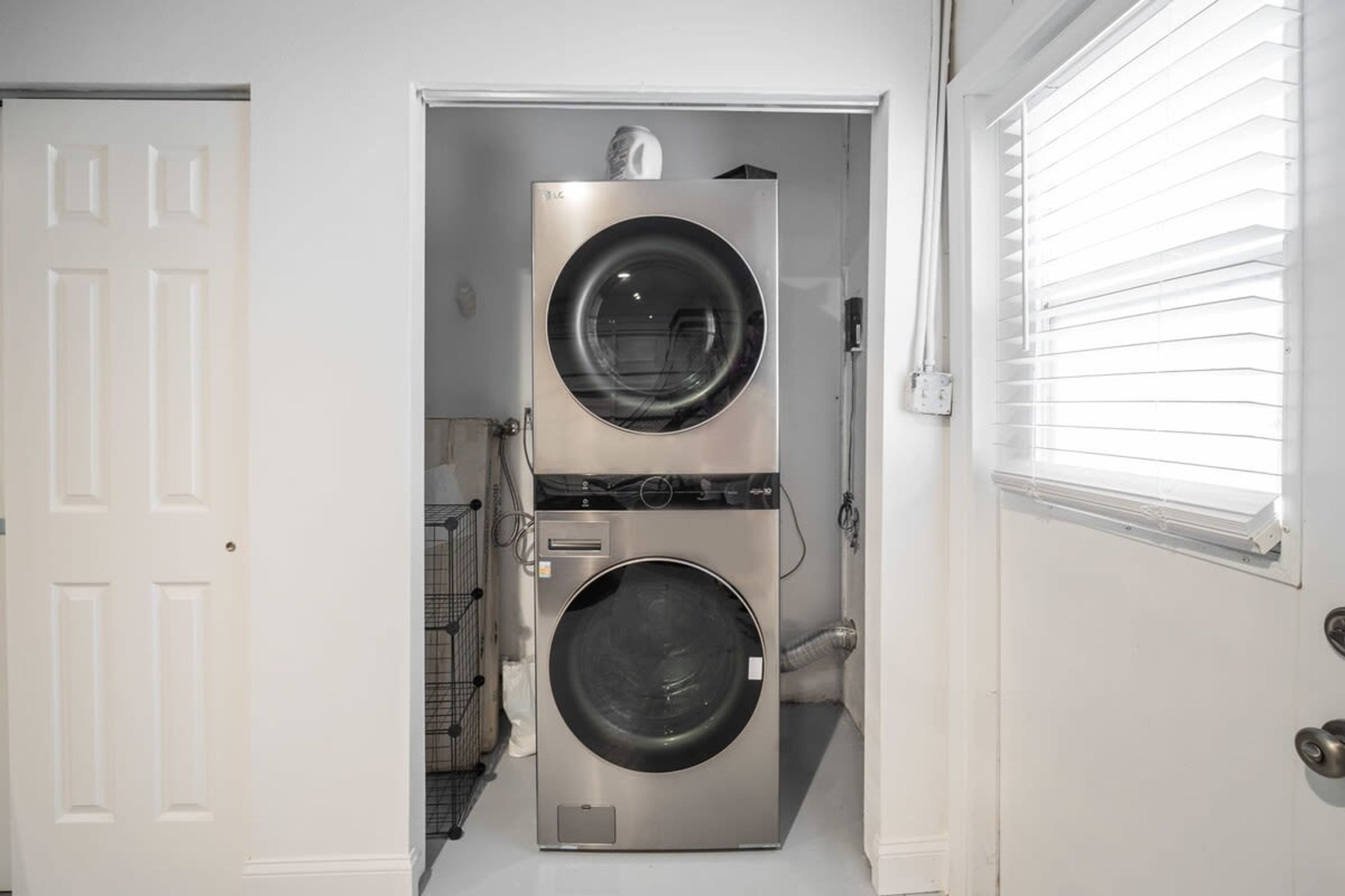 Un lavadero con dos lavadoras apiladas, un tendedero de metal y una puerta que da a otra habitación.
