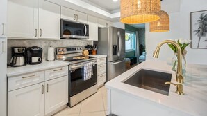 Uma cozinha moderna com armários brancos, eletrodomésticos de aço inoxidável e uma ilha grande com pia.