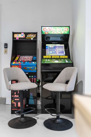 Zwei Spielautomaten mit Sitzgelegenheiten davor, einer beschriftet mit 'Class of '88' und der andere mit 'Arcade Up'.