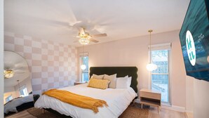 Quarto com cama grande, ventoinha no teto, televisão e janela com vista.