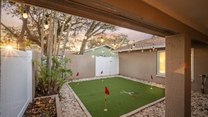 Um quintal com um campo de golfe, cerca branca e árvores.
