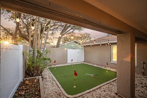 Ein Garten mit Putting-Green, weißem Zaun und Bäumen.