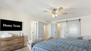 Ein Schlafzimmer mit einem Bett, einem Schminktisch, einem Fernseher und einem Deckenventilator.