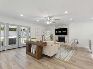 A modern living room with a fireplace, a ceiling fan, and a television mounted on the wall. - Sonoran Sunset Retreat Pool Games (Scottsdale)