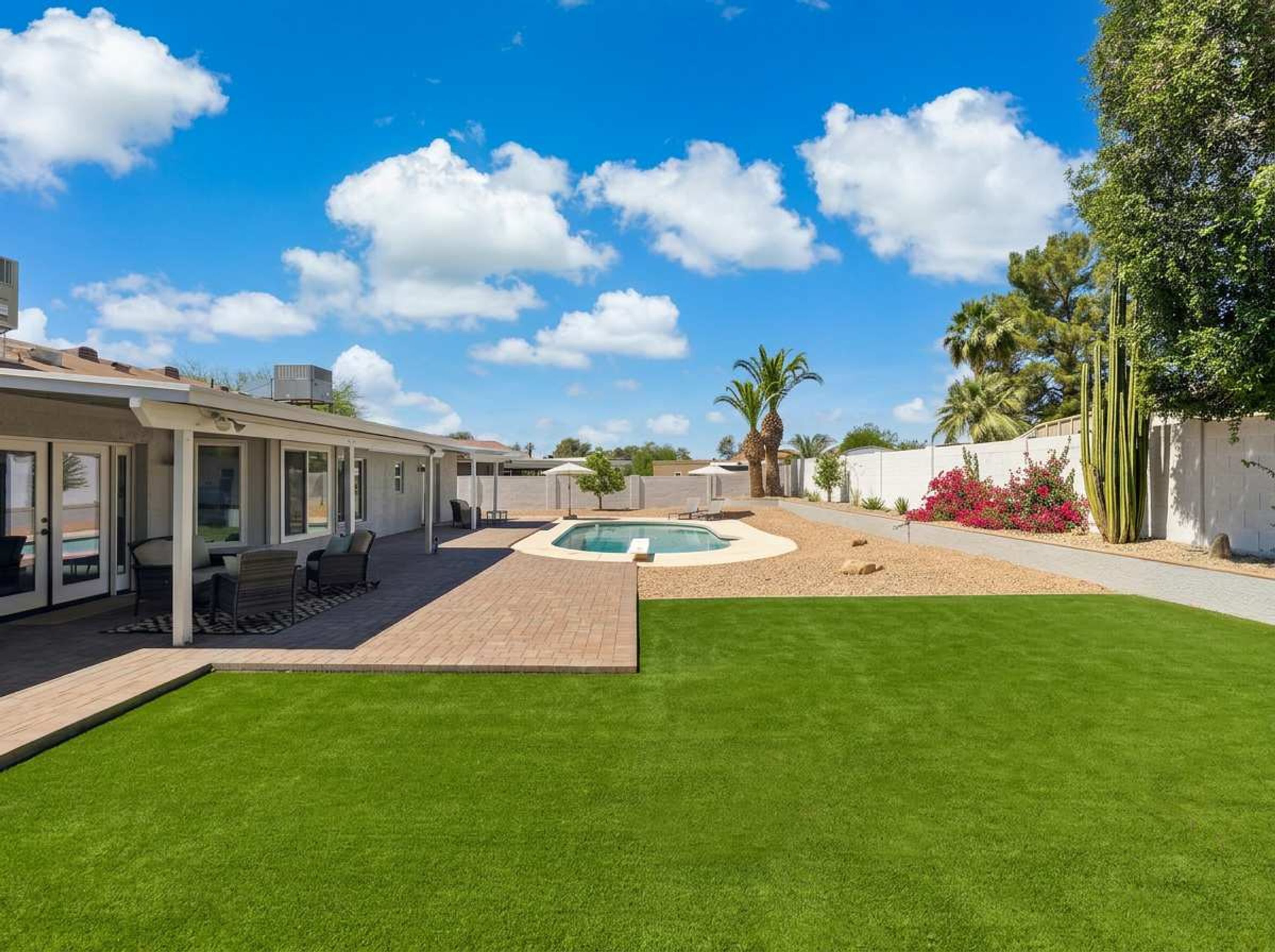 A residential property with a swimming pool, patio furniture, and a well-maintained lawn.