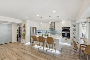 A modern kitchen with white cabinetry, stainless steel appliances, and a central island with bar stools. - Sonoran Sunset Retreat Pool Games (Scottsdale)