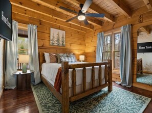 A wooden cabin bedroom with a bed, a ceiling fan, and a window with curtains. - Best of Blue Ridge Hot Tub Games Pickleball (Cherry Log)