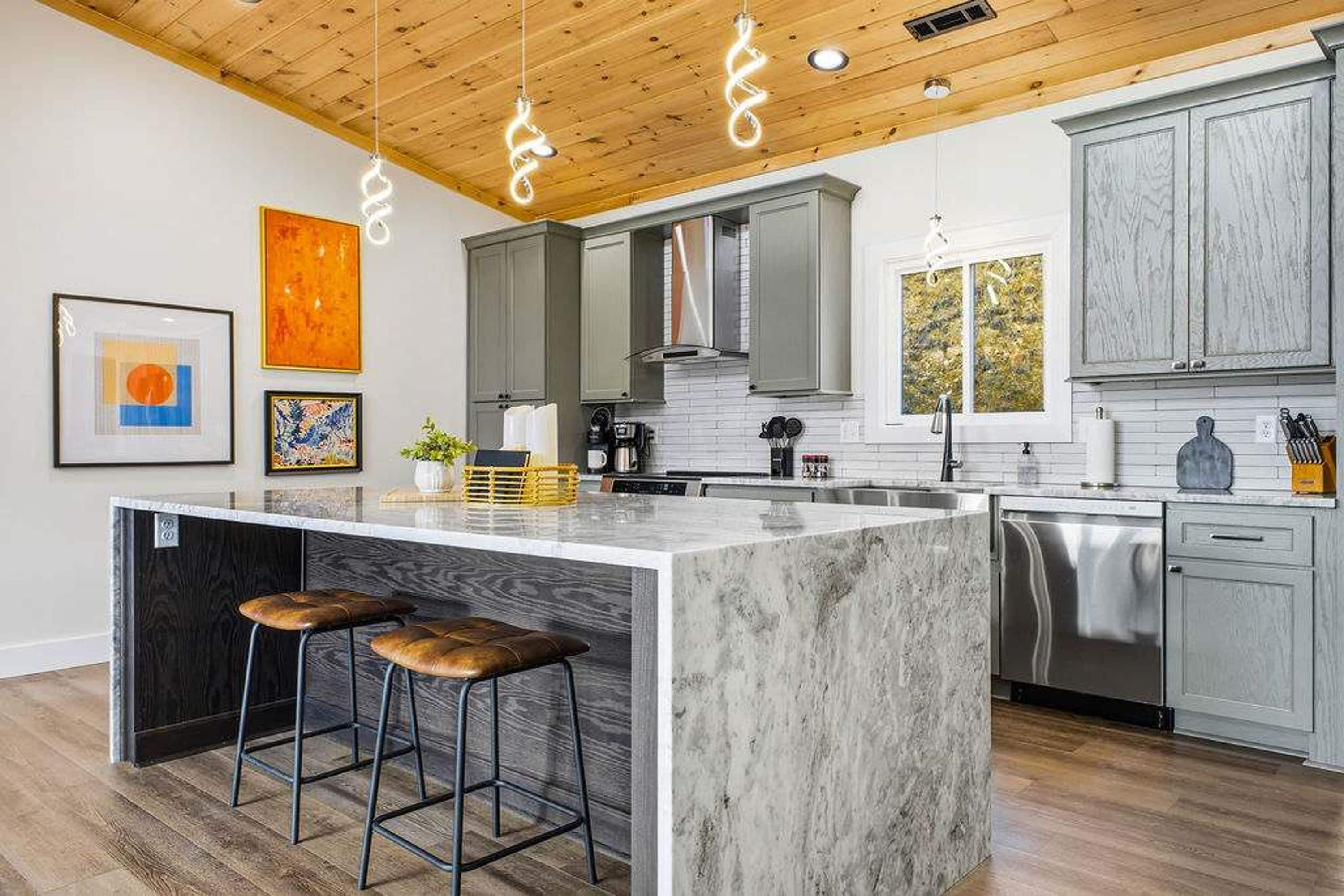 A modern kitchen with a large island, bar stools, and pendant lighting.