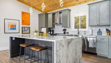 A modern kitchen with a large island, bar stools, and pendant lighting.