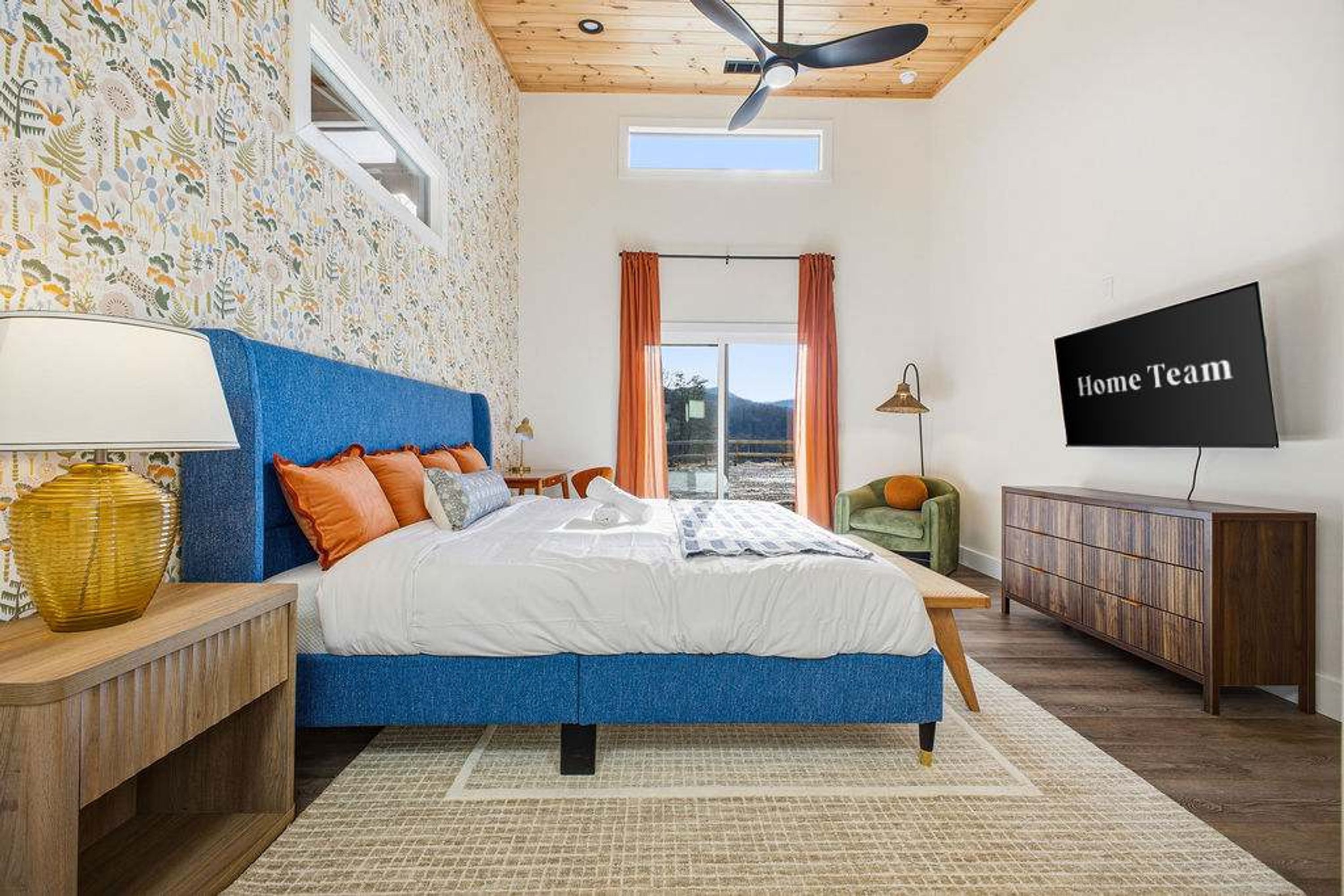 A bedroom with a large bed, a ceiling fan, a TV, and a view of the outdoors.