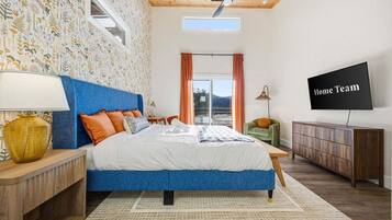 A bedroom with a large bed, a ceiling fan, a TV, and a view of the outdoors.