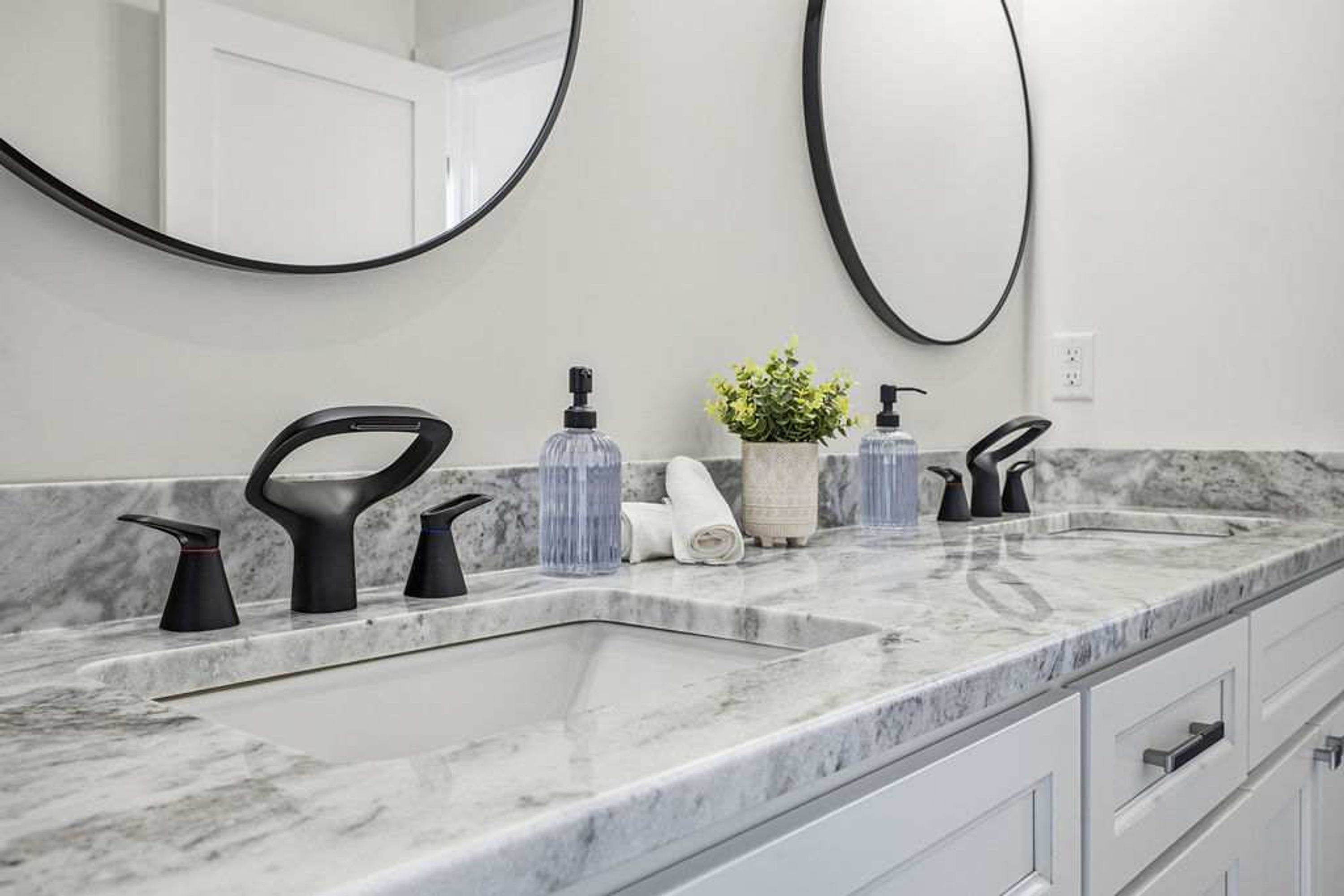 A bathroom with two sinks, black faucets, a marble countertop, a potted plant, and a towel.